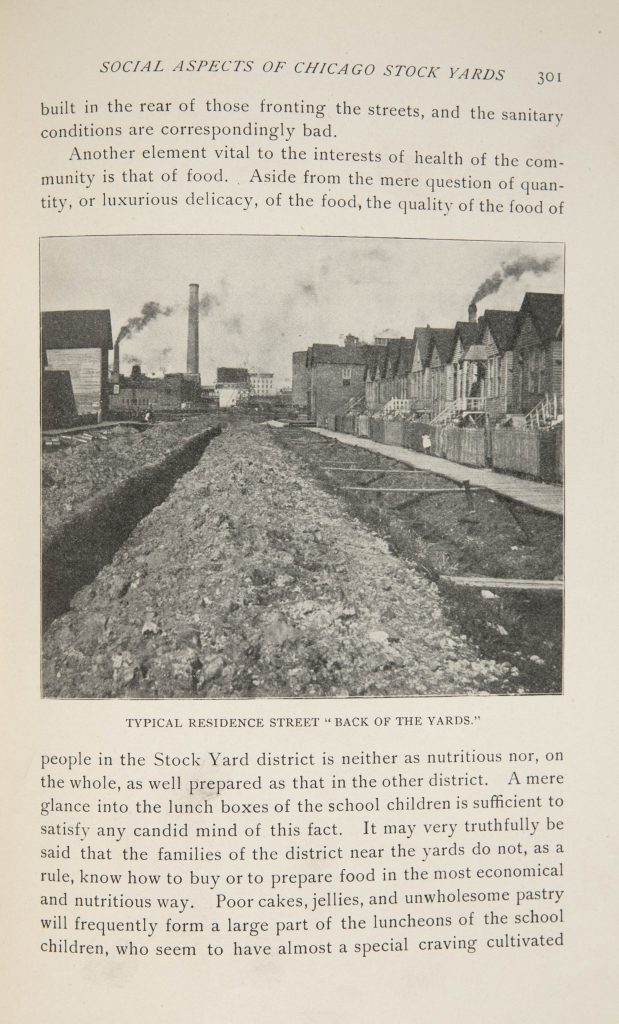 Single page of printed text with a black-and-white photo showing a row of single-story houses which open onto a plank sidewalk beside a trench of waste.