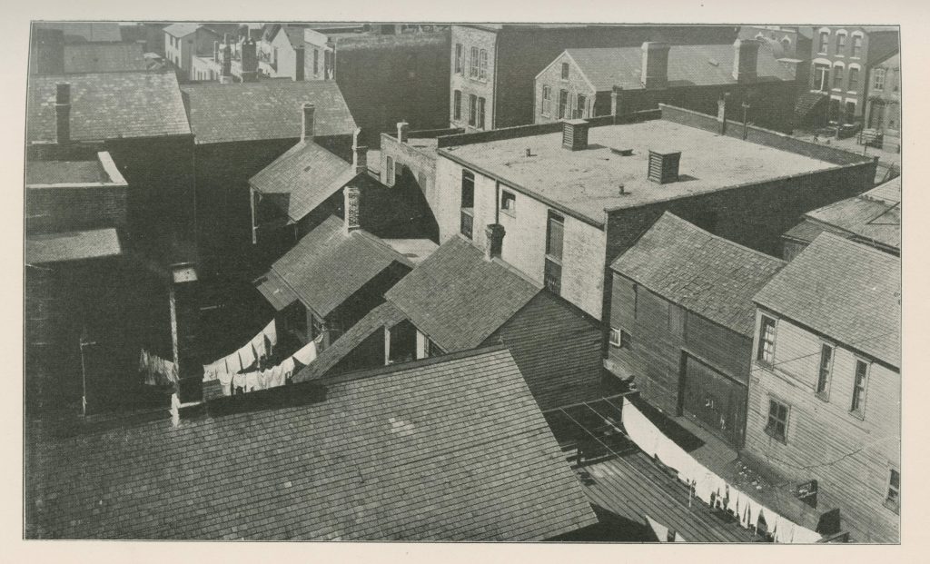 Black-and-white photo looking down on a neighborhood of tightly packed two-story houses, some with laundry hanging outside.