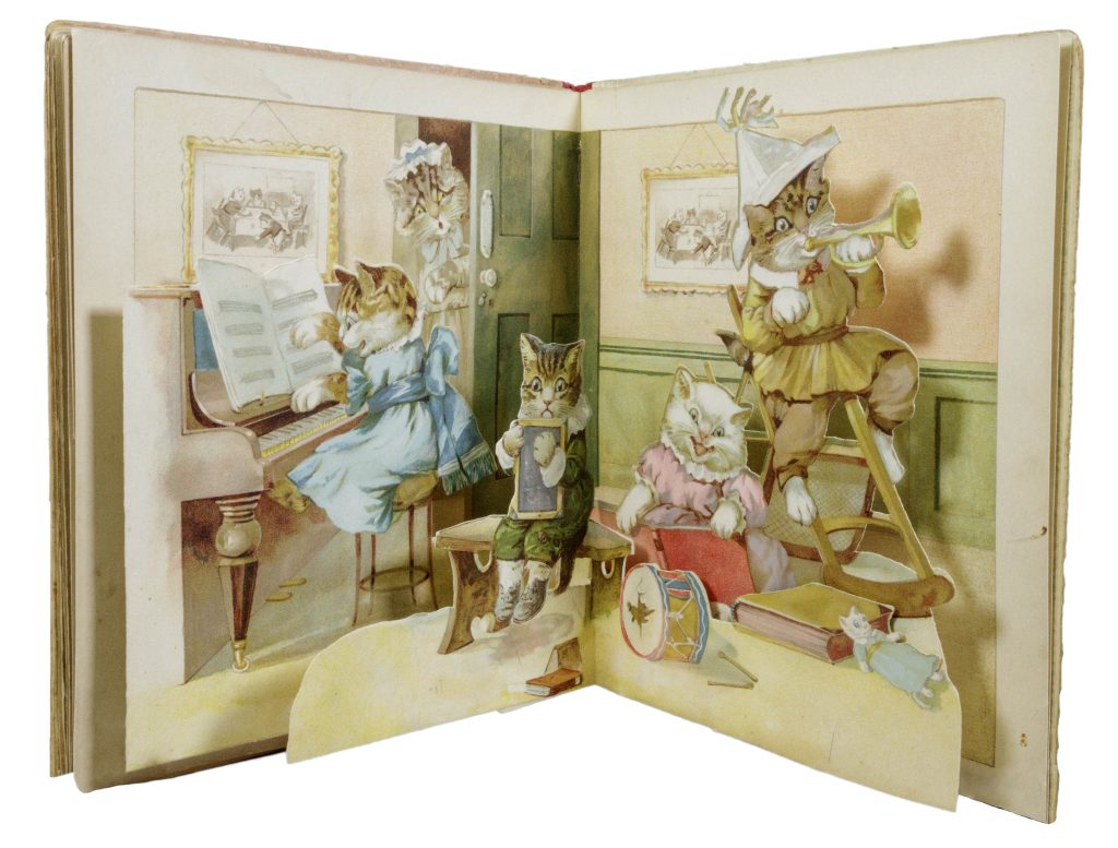 Book open to a page with a pop-out. The full-page illustration shows for kittens dressed in period clothes playing in a room. From left to right, a tabby kitten in a blue dress plays the piano; a tabby kitten in a green shirt and pants holds a small chalkboard; a white kitten in a pink dress reads a book; and a tabby kitten in beige pants and shirt sits at the top of a small ladder blowing a horn and wearing a folded paper hat. Other toys are scattered on the floor. In the background an adult gray cat in a maid's uniform looks through the room's partly-open door in dismay.
