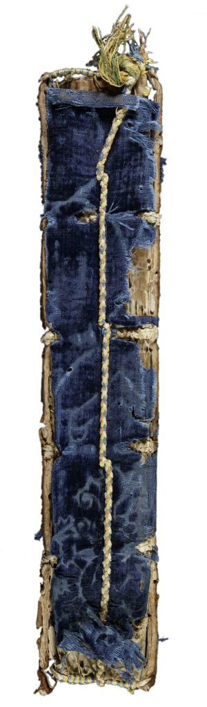 Spine of a manuscript book bound in blue velvet printed with floral design. The velvet has worn away on the edges of the spine revealing the board beneath. A braided cord of blue, yellow, and orange runs down the center of the spine.