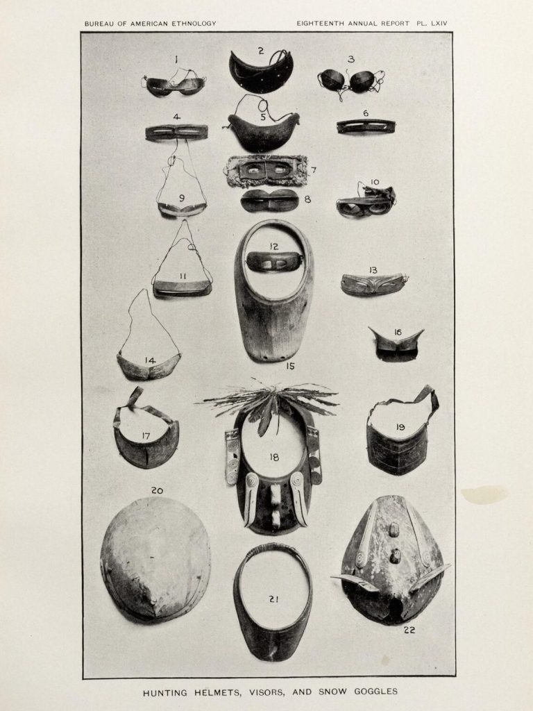 Black-and-white photograph of an array of traditional helmets and snow goggles used by the Indigenous people of the Bering Strait.