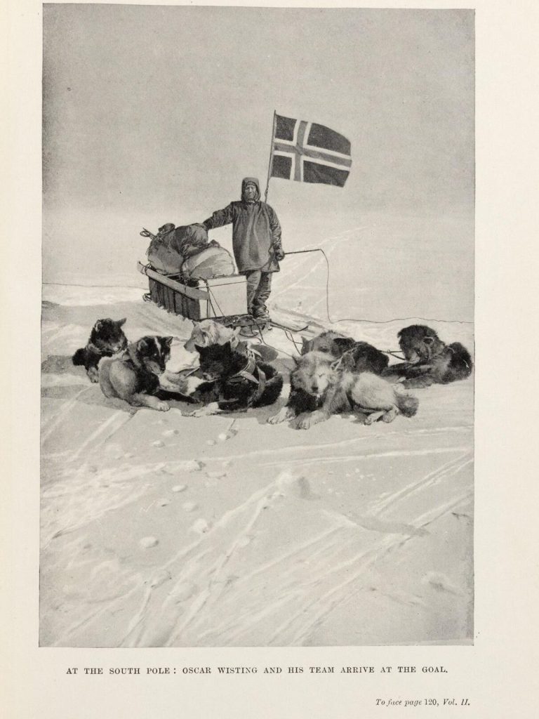 Black-and-white photograph of a European man in polar gear posing with a sled dog team and the Norwegian flag. Captioned: "At the South Pole" Oscar Wisting and this Team Arrive at the Goal"