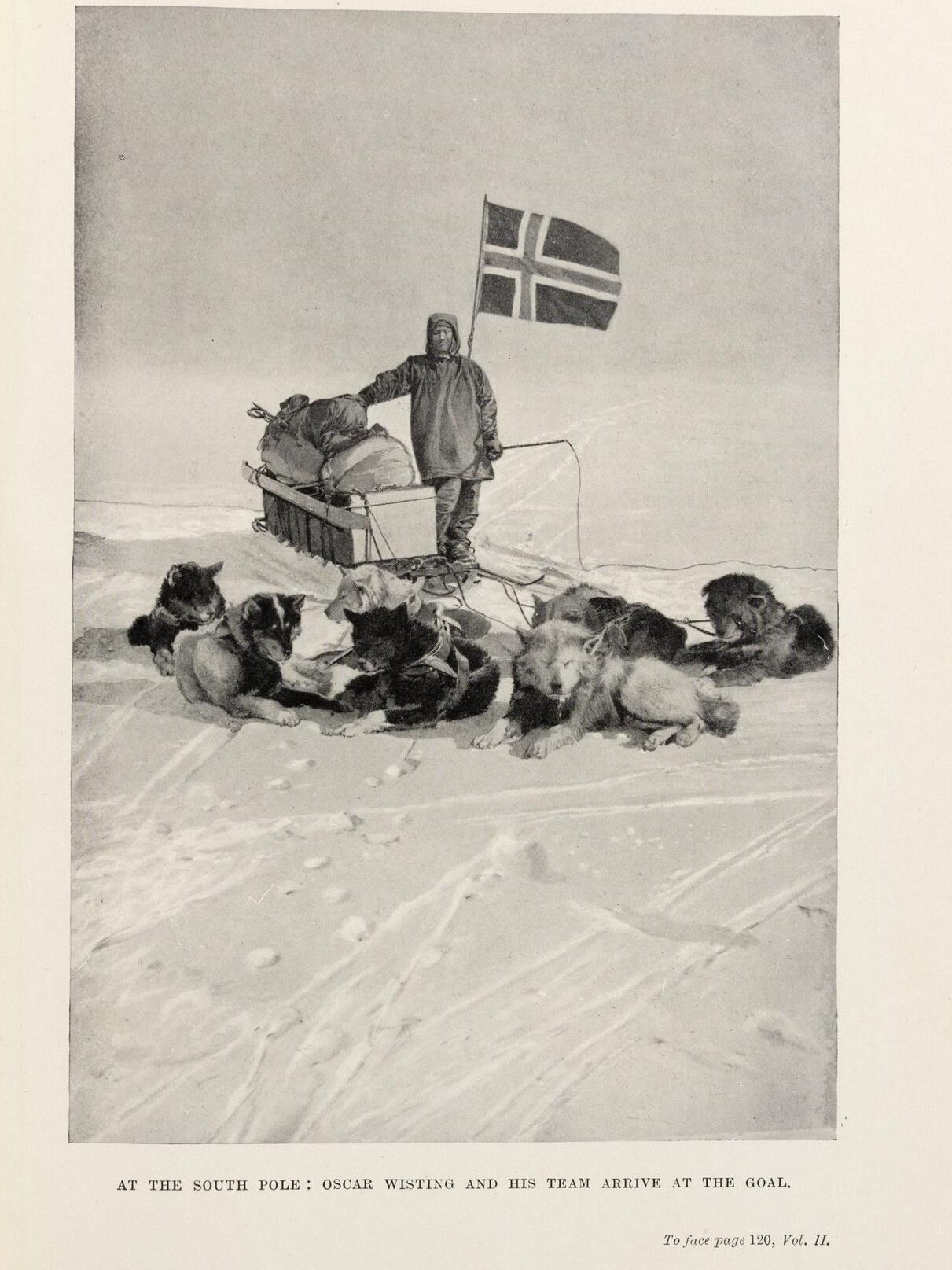 Black-and-white photograph of a European man in polar gear posing with a sled dog team and the Norwegian flag. Captioned: "At the South Pole" Oscar Wisting and this Team Arrive at the Goal"