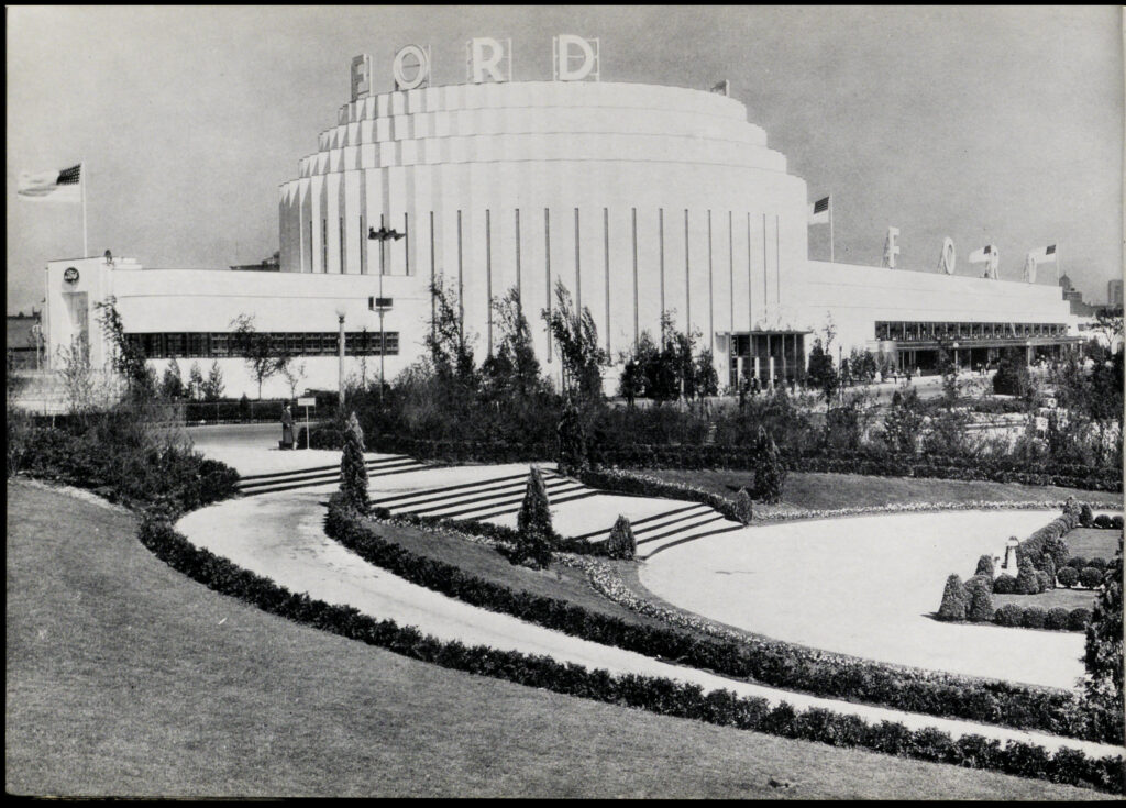 Black-and-white photo of the Ford Building at the Century of Progress. It is a white building with a tall central rotunda and two lower rectangular wings. The rotunda says "FORD" in large letters on its roof. The building is set in landscaped gardens.