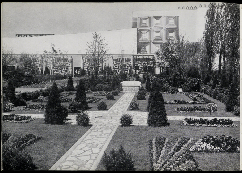 Black-and-white picture of the Oak Park Garden from the Century of Progress. This is a Victorian formal garden laid out in a square around a fountain with carefully symmetrical shrubs and flowers. An Art Deco greenhouse is in the background.