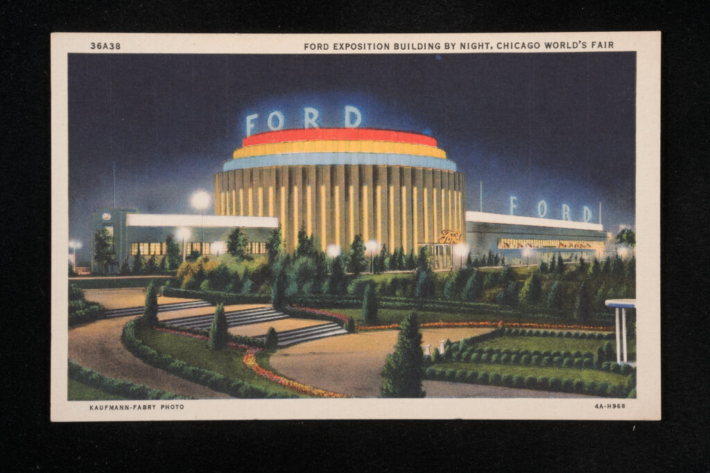 Painted postcard image of a large white, blue, red and yellow building lit up at night. It has a circular middle section and long wings on each side. Large letters spell out "FORD" on top of the center circular section.