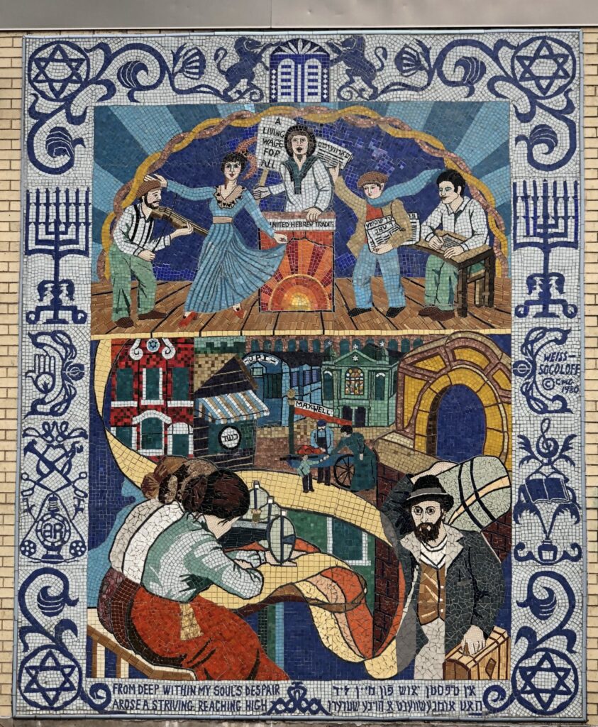 Multi-colored tile mosaic depicting the lives of Jewish immigrants in Chicago in the early 20th century. At the top of the image, a woman with a protest sign lectures at a podium. On one side of her a man and a boy write and sell newspapers. On other side, a man plays a fiddle with a woman dances. Below them, women work at sewing machines, while the textile they make becomes the road of Maxwell Street. Peddlers and immigrants push carts and carry baggage down the road. Around the image is a boarder with symbols of Jewish culture, including the Start of David, menorahs, the Ten Commandments, ink wells, books, and music notes. At the bottom is the phrase "From deep within my soul's despair arose a striving reaching high" in English and Yiddish.