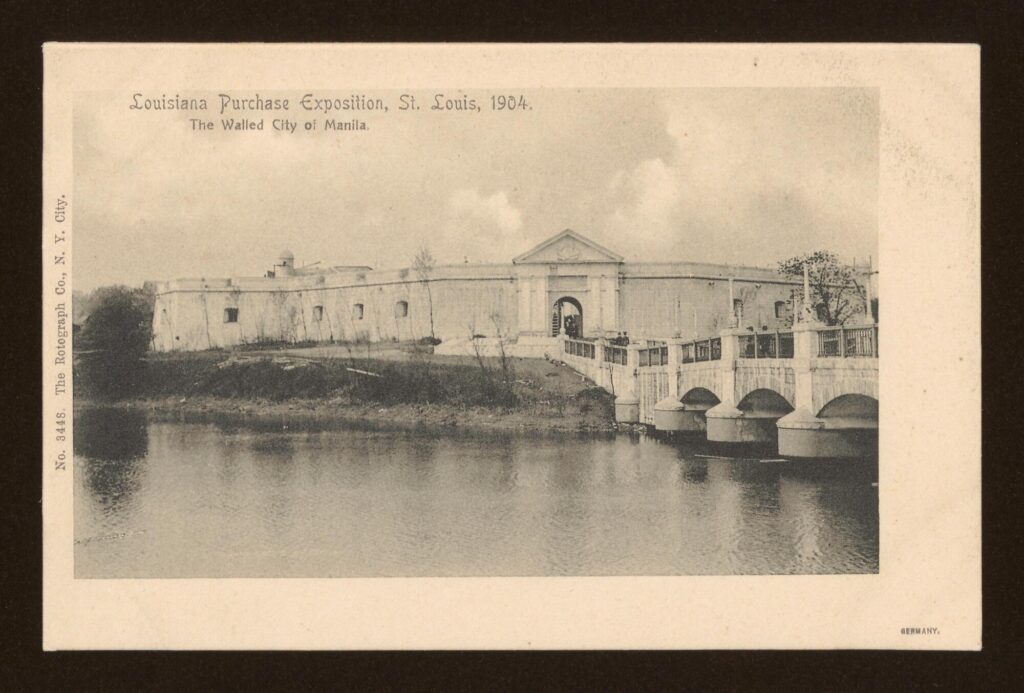 Black-and-white photo postcard showing a temple-front at the entrance next to a river with a bridge.