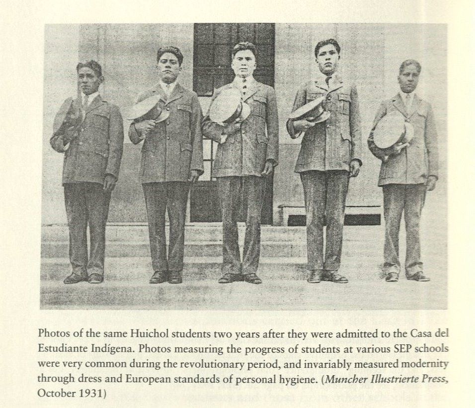 Black-and-white photo of four five Huichol boys standing on the steps of a building. They wear military-style suits and hold their hats against their chests in a salute. Below the image is the caption, "Photos of the same Huichol students two years after they were admitted to the Casa del Estudiante Indígena. Photos measuring the progress of students at various SEP schools were very common during the revolutionary period, and invariably measured modernity through dress and European standards of personal hygiene. (Muncher Illustrierte Press, October 1931).