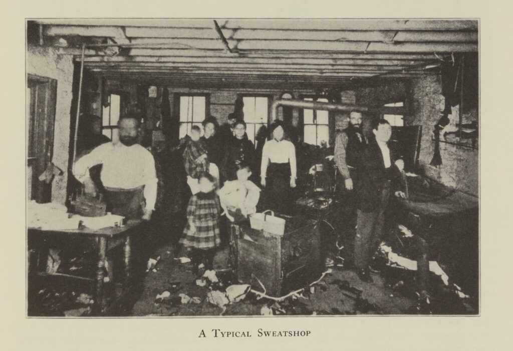 A black-and-white photograph of a cramped, dark room with a handful of people, mostly adults but some children. They appear to be working on textile.
