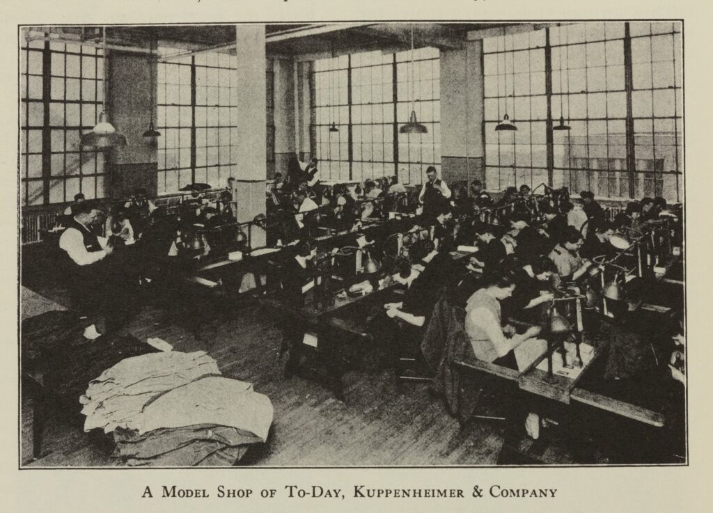 Black-and-white photo of a large room with rows of people working at machines. The floor is clean, and the room has a high ceiling and large windows.