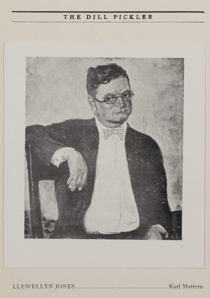 Portrait of Llewellyn Jones, a clean-shaven white man with a round face and round glasses sitting in a chair, with his arm over the back. He wears a white shirt, patterned bow tie, and dark coat and pants.