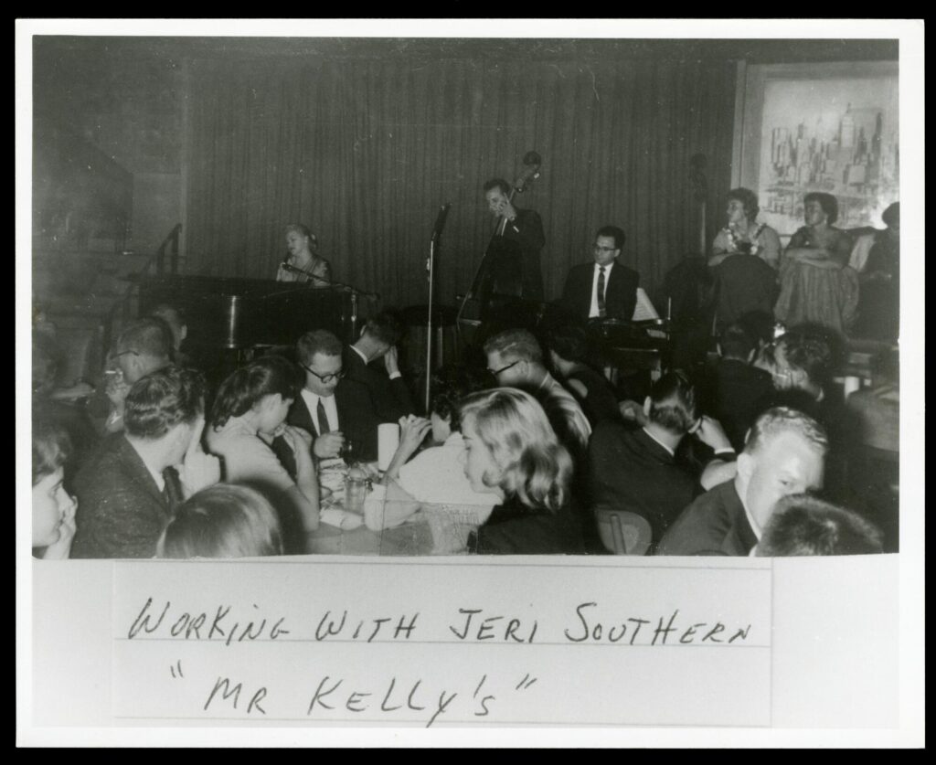 Black-and-white photograph of a crowded night club with a band on stage.