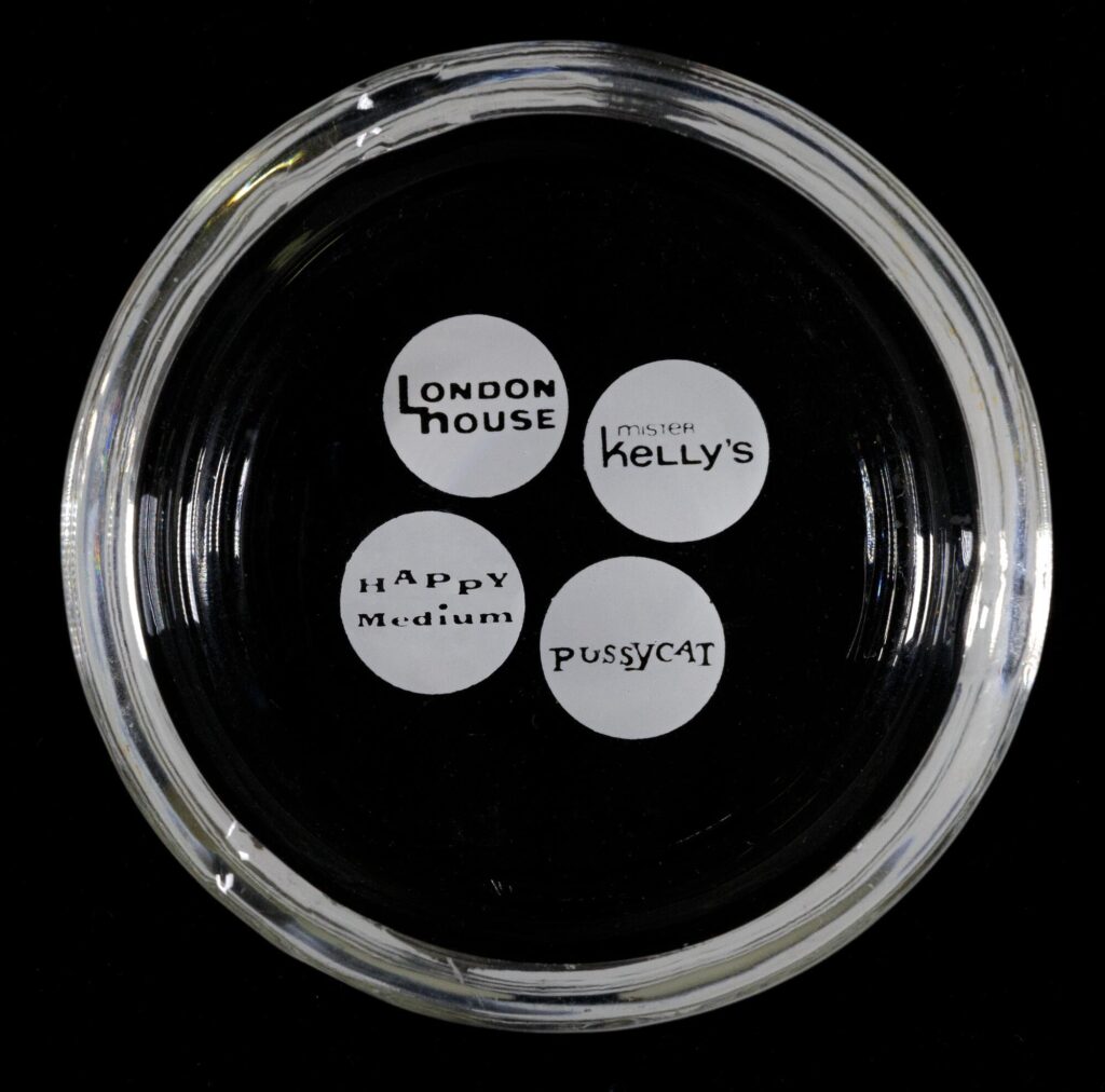 Clear ashtray on a black background with the logos of four Marienthal properties: London House, Mister Kelly's, Happy Medium, and Pussycat.