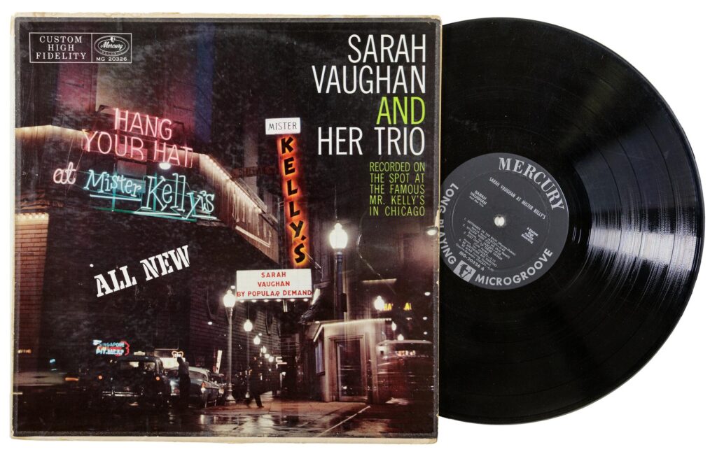 Record sleeve with a color photograph of Mister Kelly's, a two-story building on a city street corner with neon signs saying "Hang your Hat at Mister Kelly's" and "Sarah Vaughan by Popular Demand." The black record sticks partly out of the sleeve.